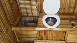 Un WC in legno con interni in bambù, una scopa e un piccolo cestino.