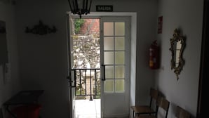 A room with a door labeled 'SALIDA' leading to an outdoor area with a stone wall and a tree. There are two wooden chairs and a red chair in the room. - Pension Rural Areal (Padron)