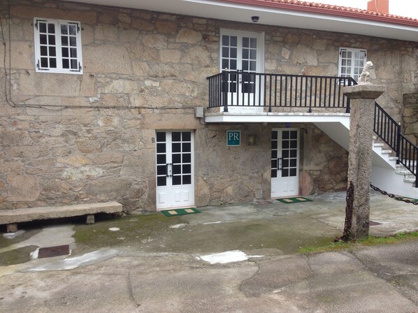 A stone building with a balcony, a staircase, and a sign indicating a parking area. - Pension Rural Areal (Padron)