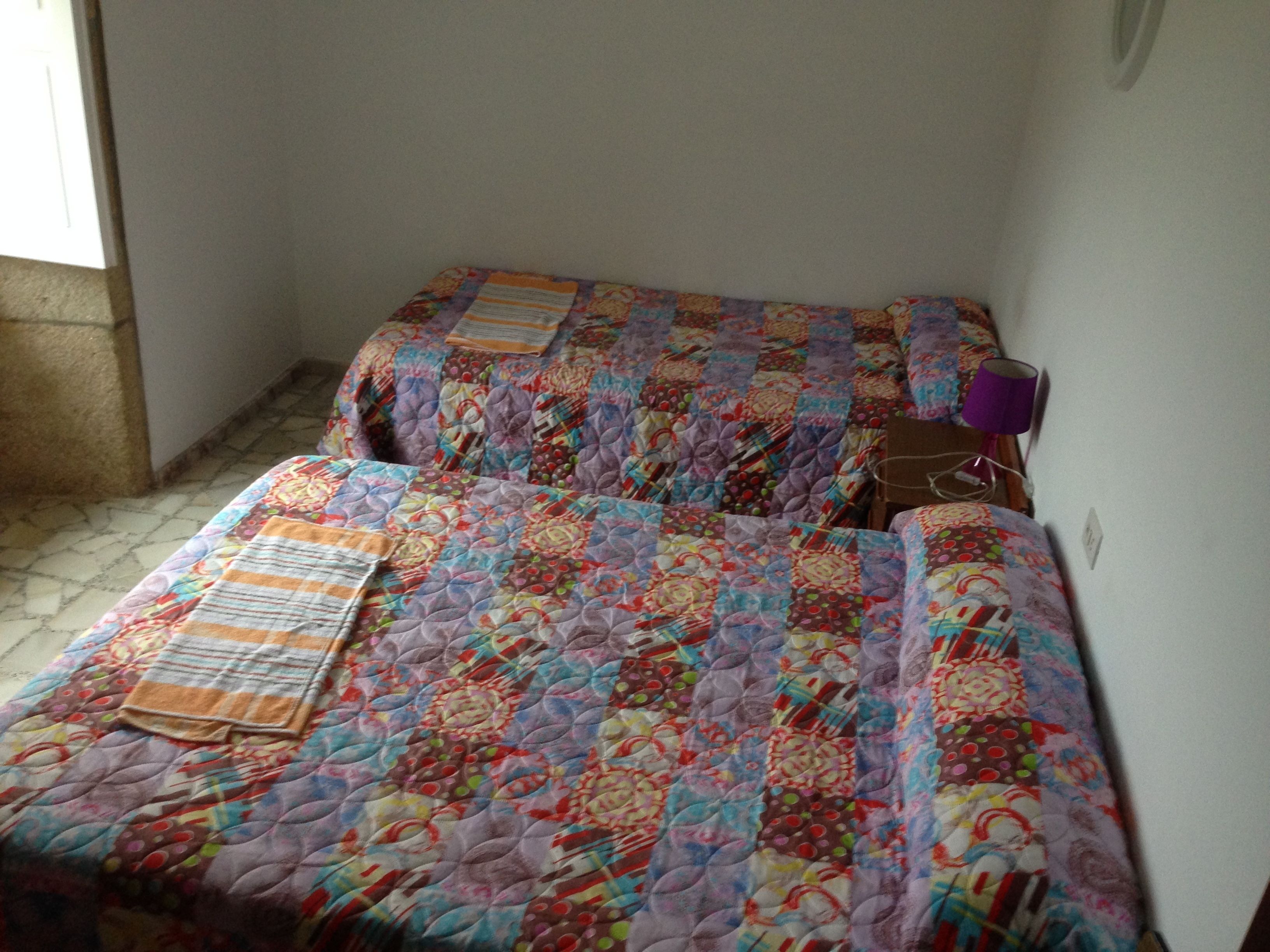 A small, cozy room with two beds covered in colorful quilts.