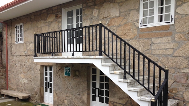 A stone building with a white exterior, a black metal staircase, and a small balcony. - Pension Rural Areal (Padron)