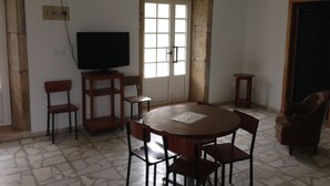 A dining area with a round table, four chairs, a television on a stand, and a window with a view of the outside. - Pension Rural Areal (Padron)