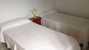A small, simple room with two single beds, a nightstand with a lamp, and a plain white wall. - Pension Rural Areal (Padron)
