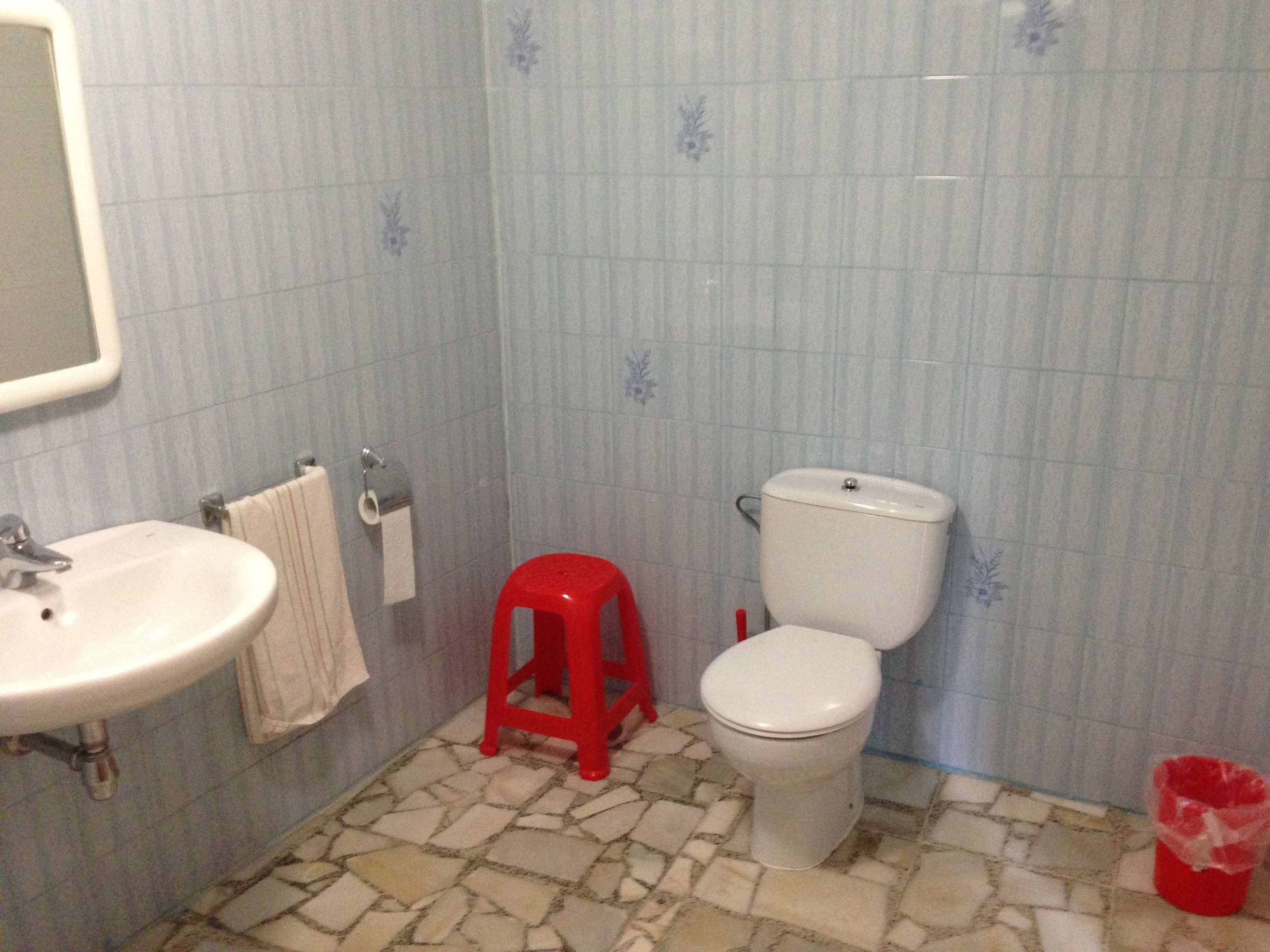 Un baño con un lavamanos blanco, un inodoro y un taburete rojo.