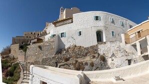 A white, curved building with a stone base, a small door, and a window with blue shutters.