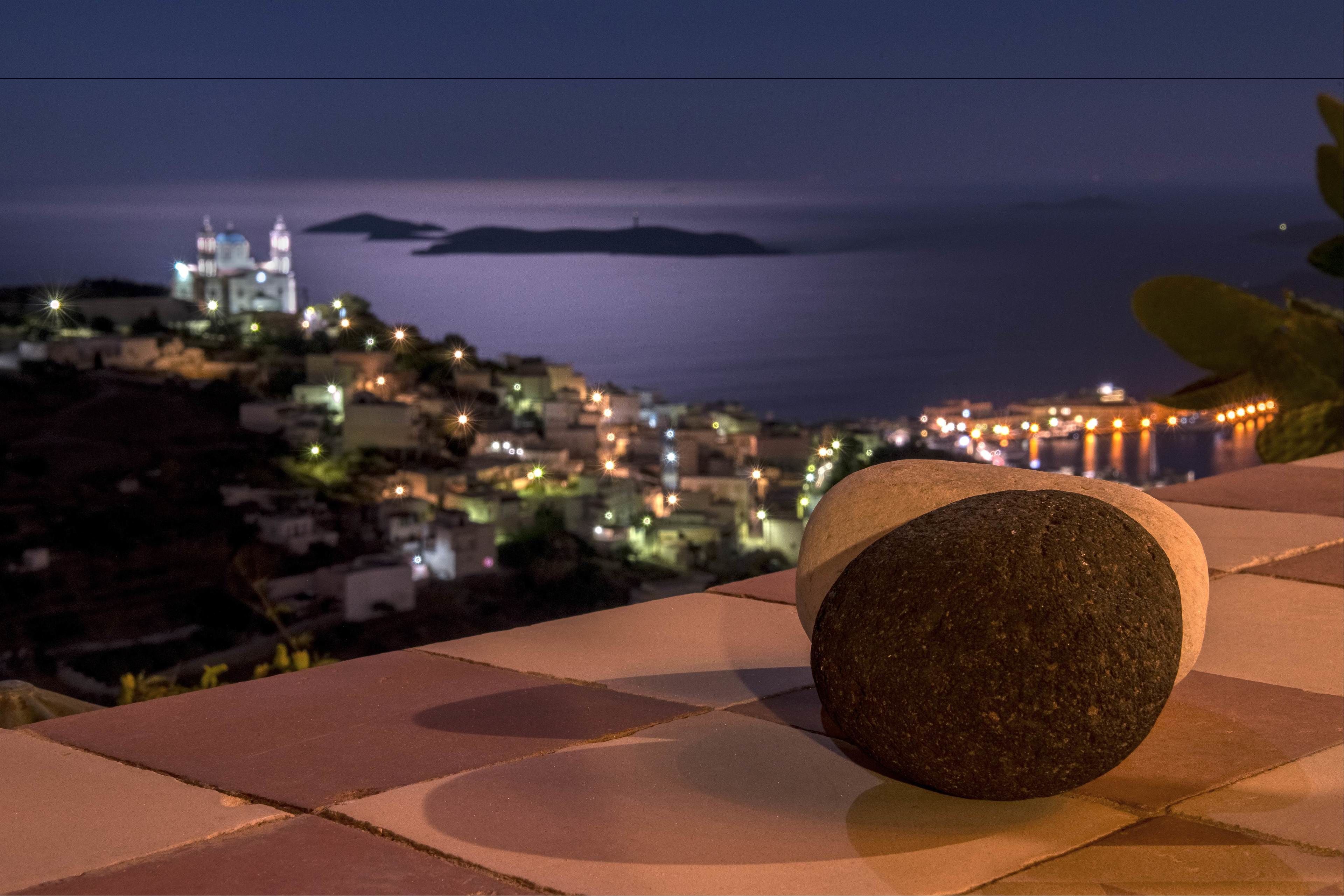 A stone bench overlooking a coastal town at night with illuminated buildings and a church.