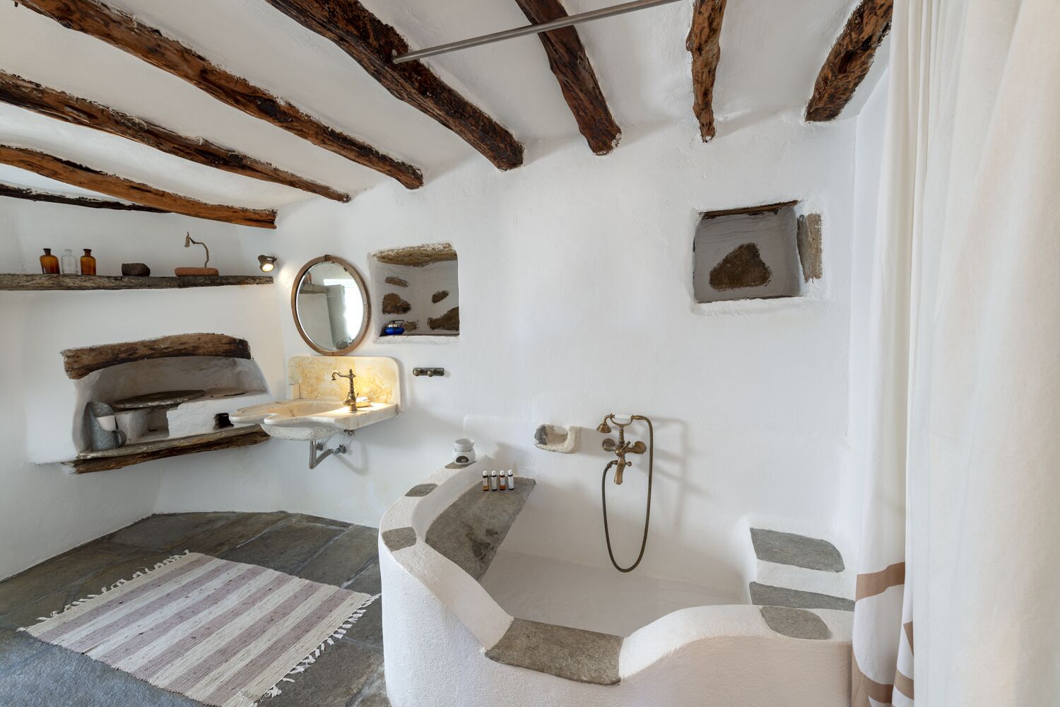A rustic bathroom with exposed wooden beams, a stone sink, a bathtub, and a striped rug.
