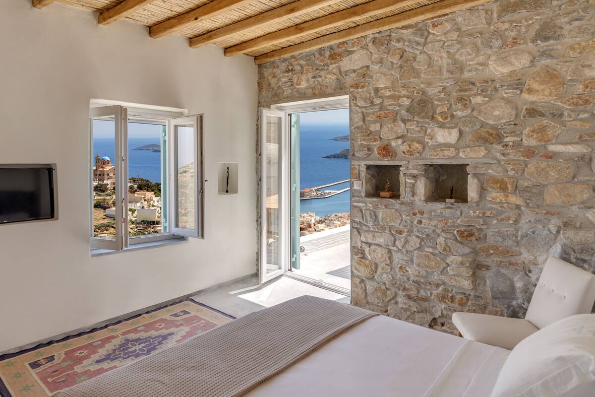Un dormitorio con pared de piedra, una cama, un televisor y vista al mar.