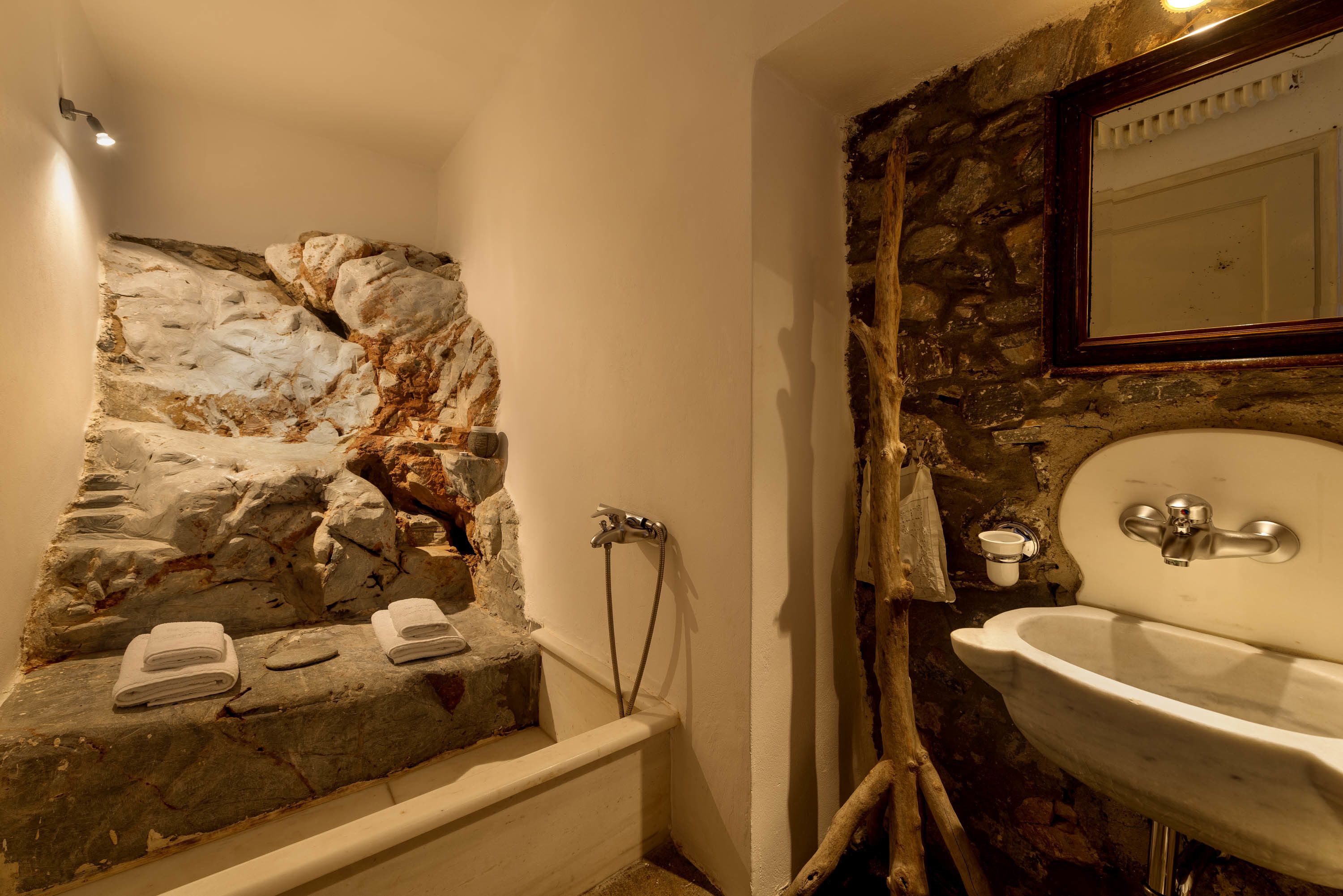 Un baño con pared de piedra, una bañera blanca y un lavabo con espejo.