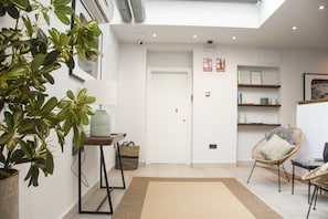 Un interior moderno con una planta en maceta grande, una mesita de madera, una silla de mimbre y una estantería.