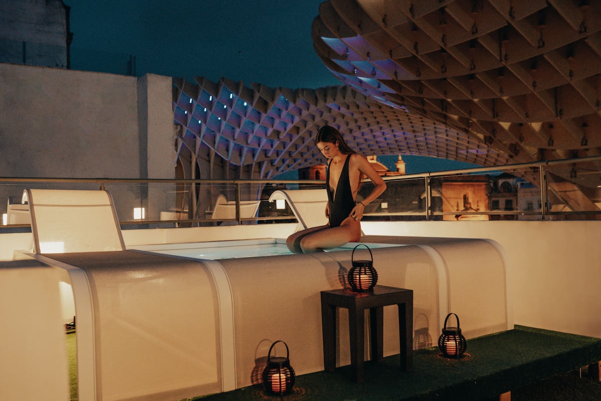 A woman sitting on a poolside lounge chair with a modern architectural backdrop.
