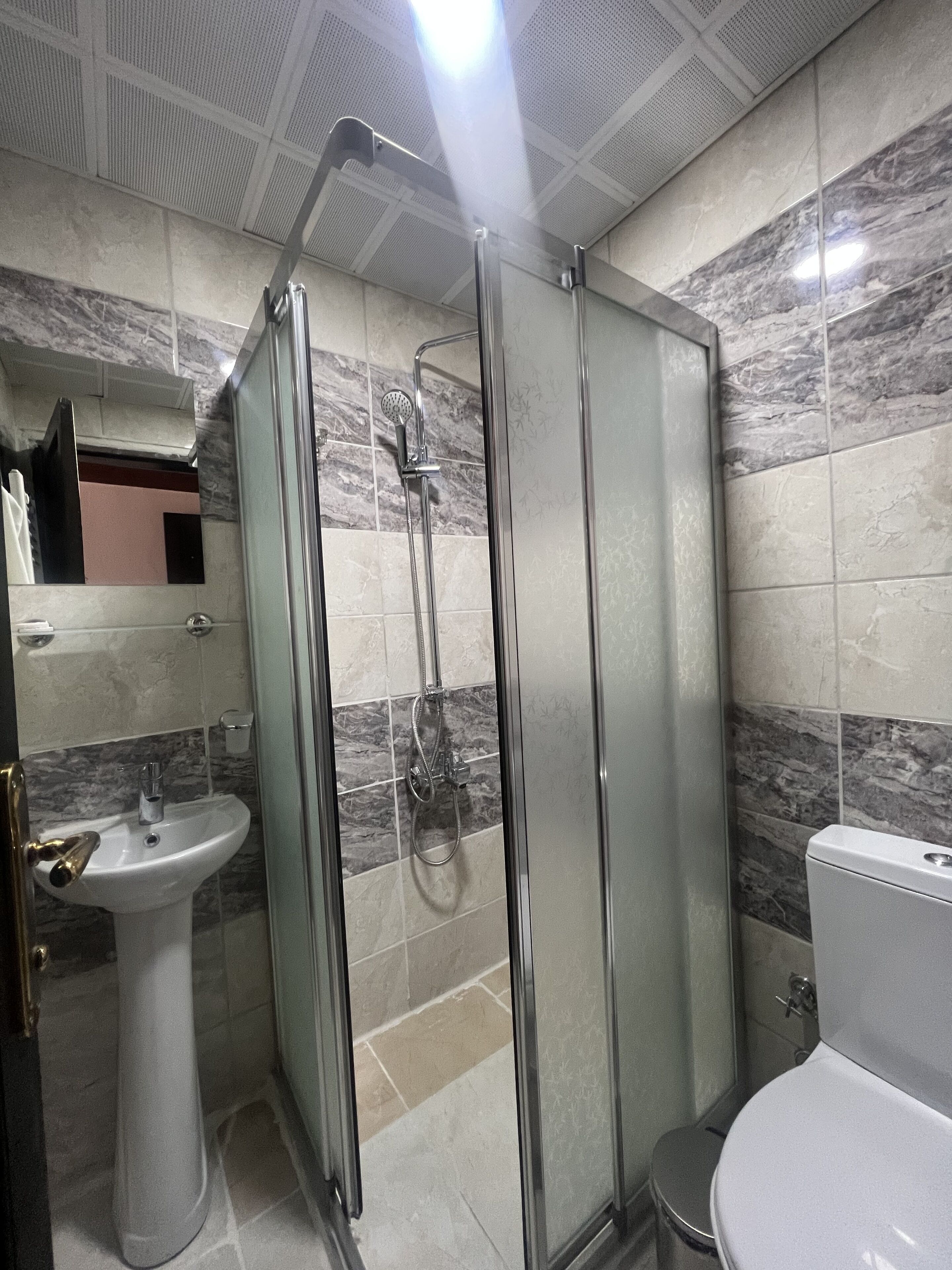Un baño con ducha de vidrio, lavamanos pedestal y retrete.