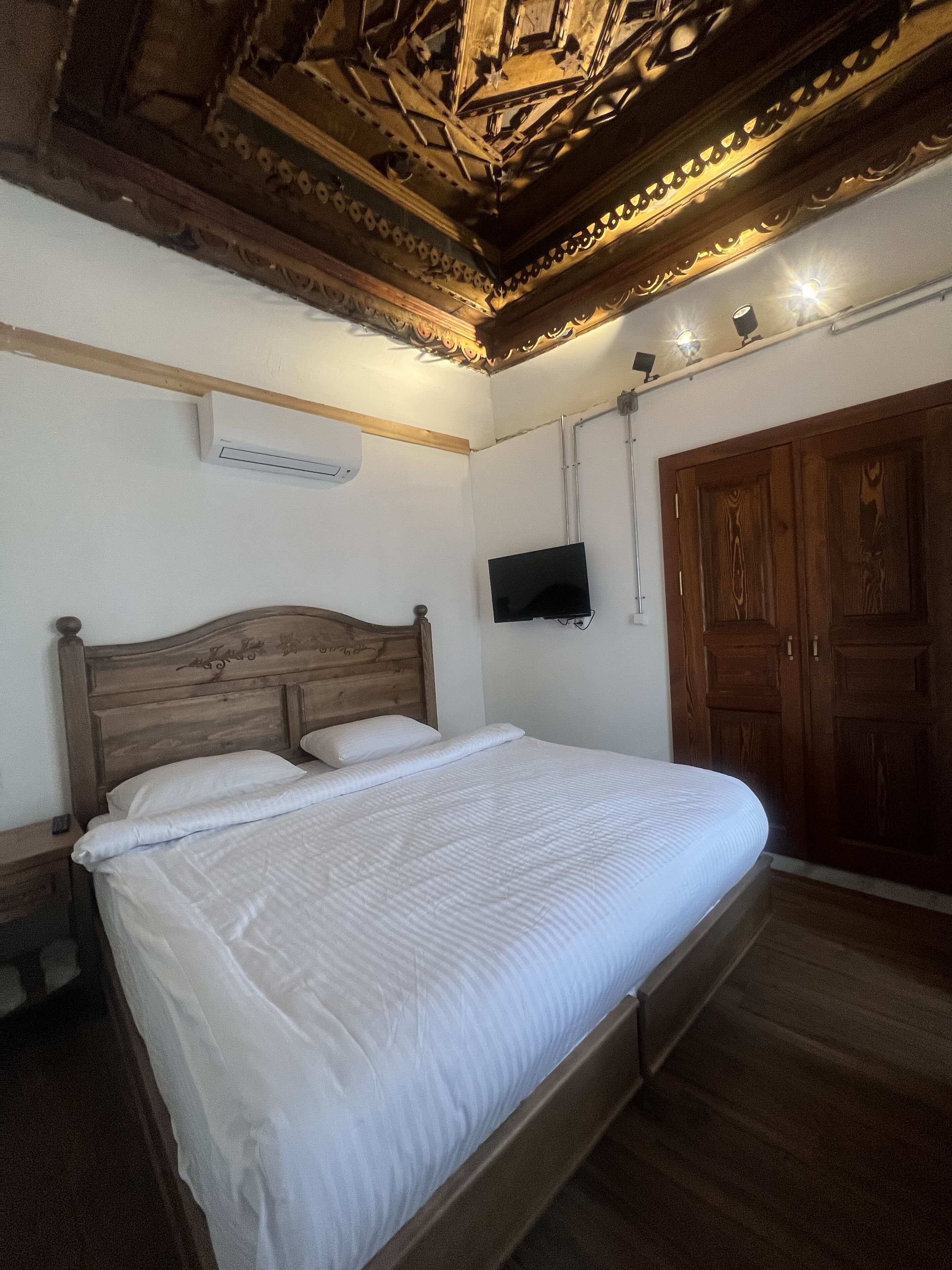 A bedroom with a wooden bed, a television mounted on the wall, and a wooden wardrobe.