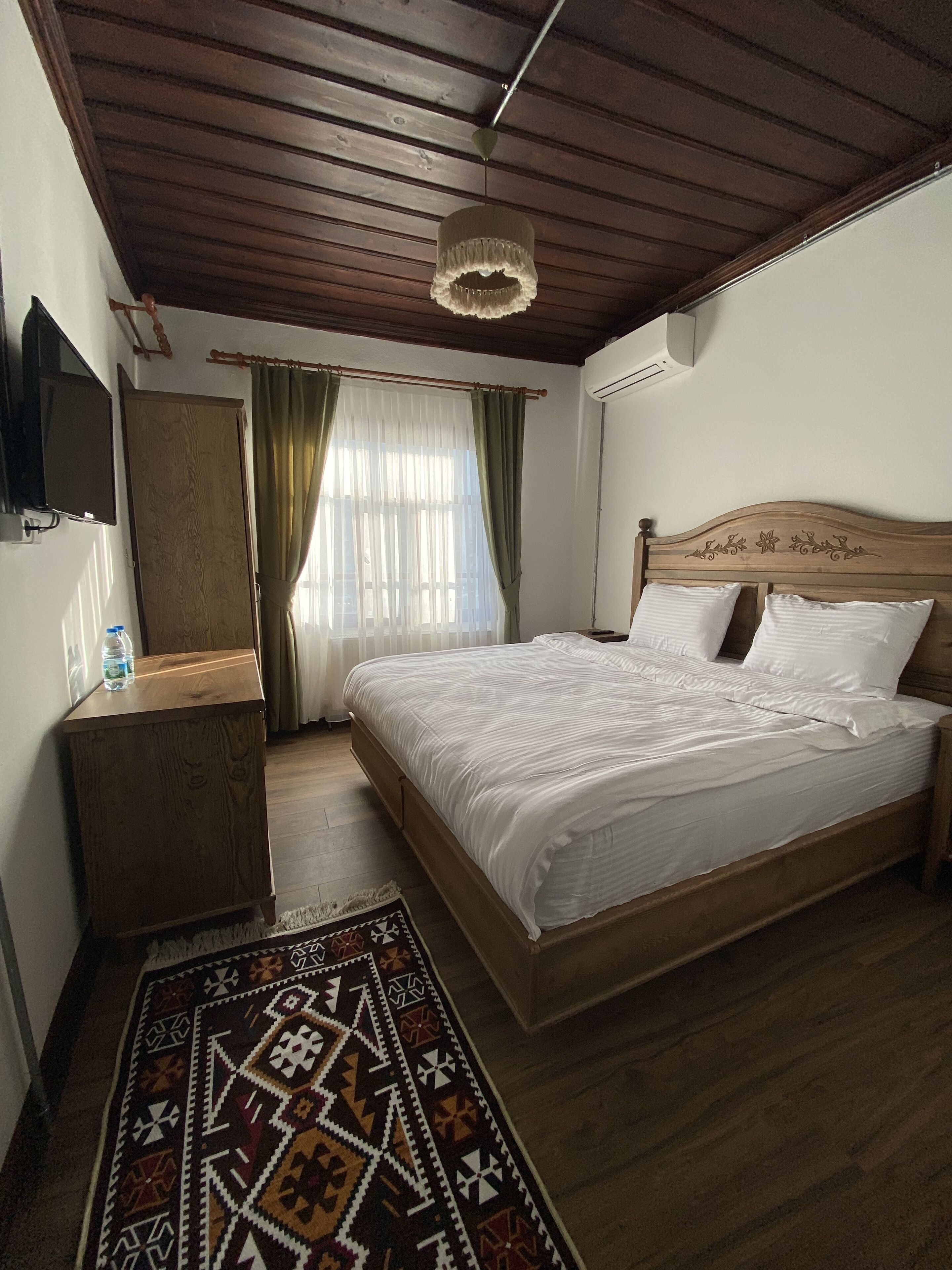 A bedroom with a wooden bed, a nightstand, a TV mounted on the wall, and a patterned rug.