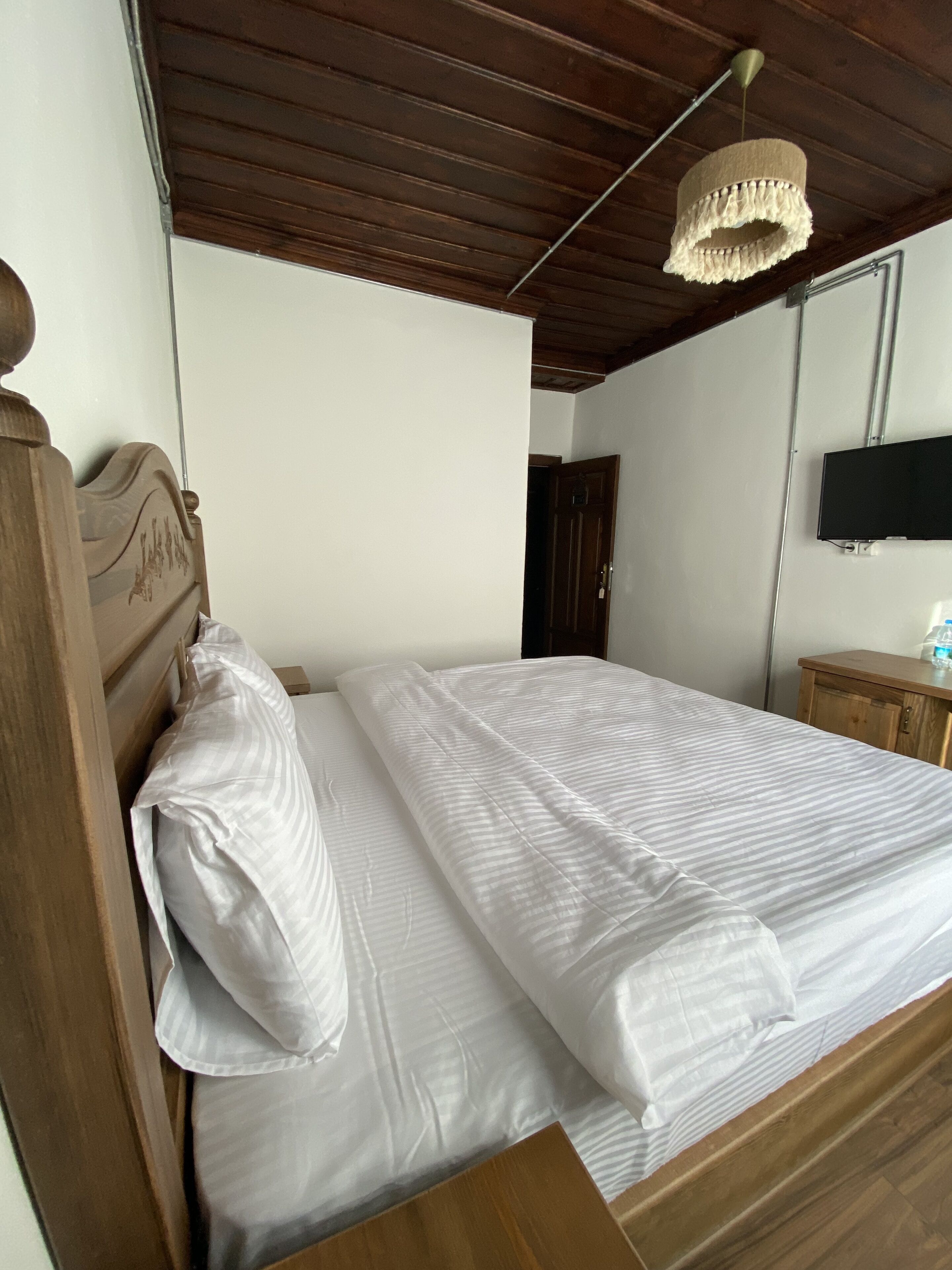 Una cama bien hecha con sábanas blancas en una habitación con vigas de madera y un televisor montado.