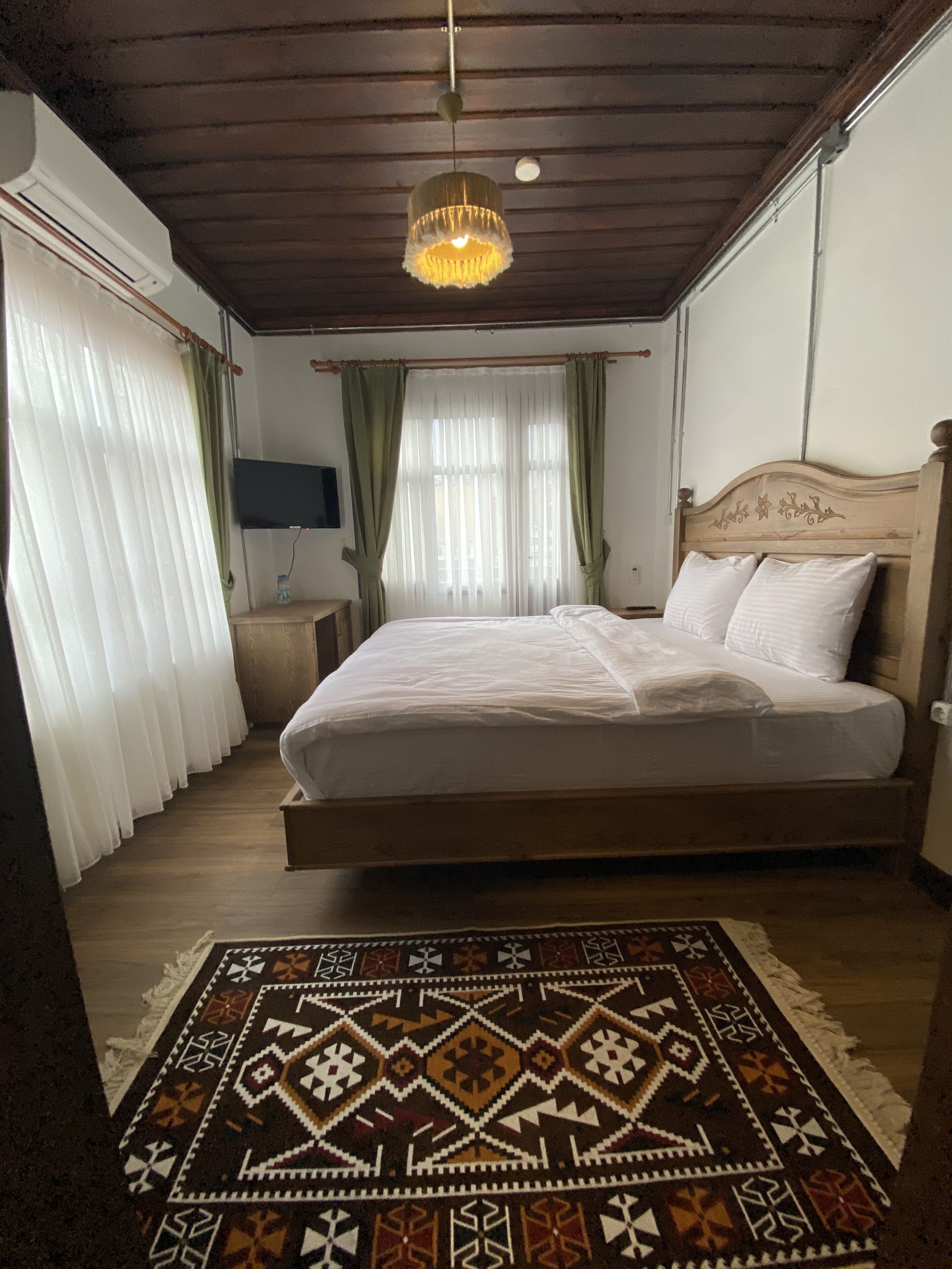 A bedroom with a wooden bed, a patterned rug, a chandelier, and curtains.