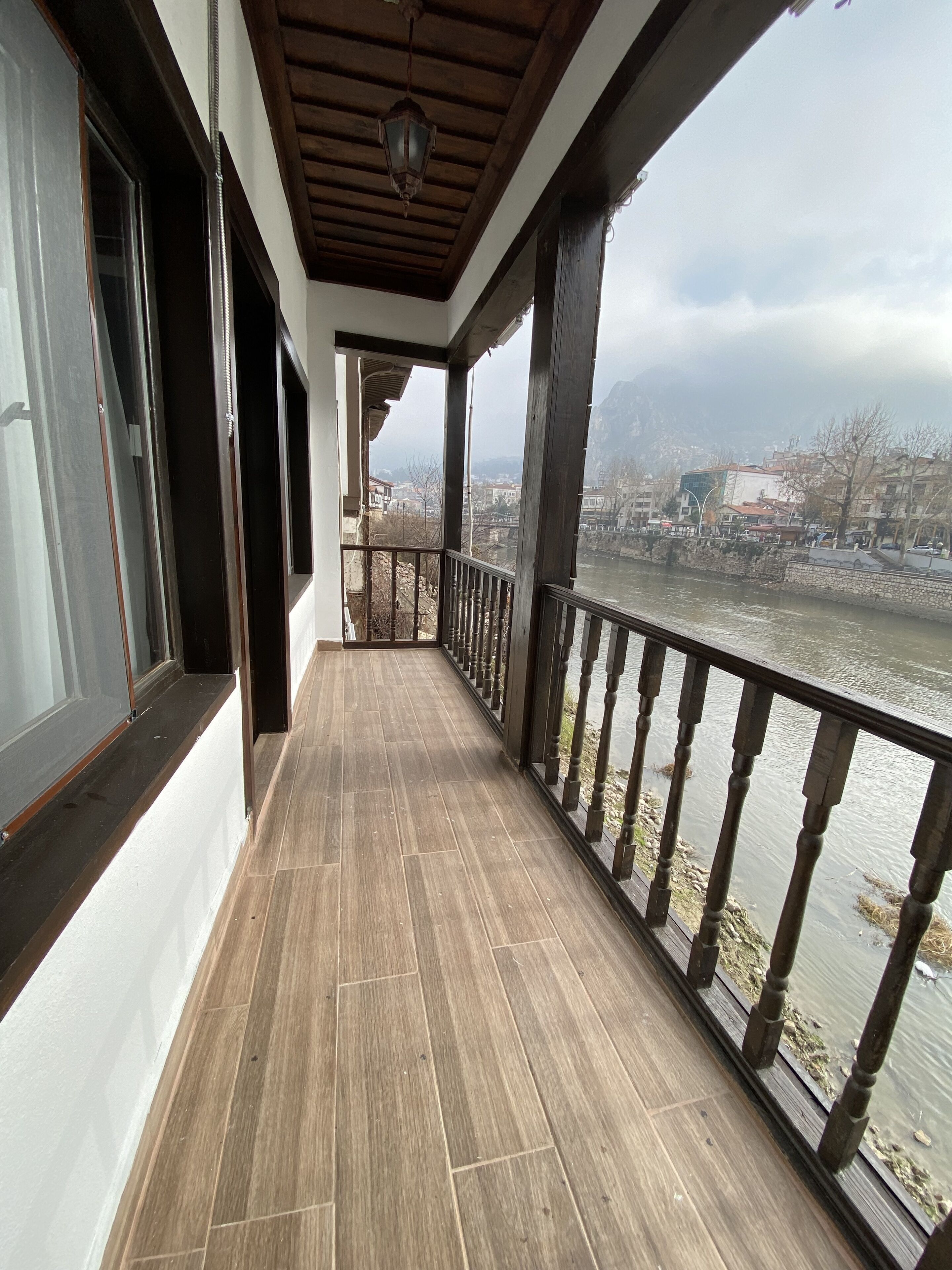 A balcony with a wooden floor, a railing, and a view of a river and buildings in the distance.