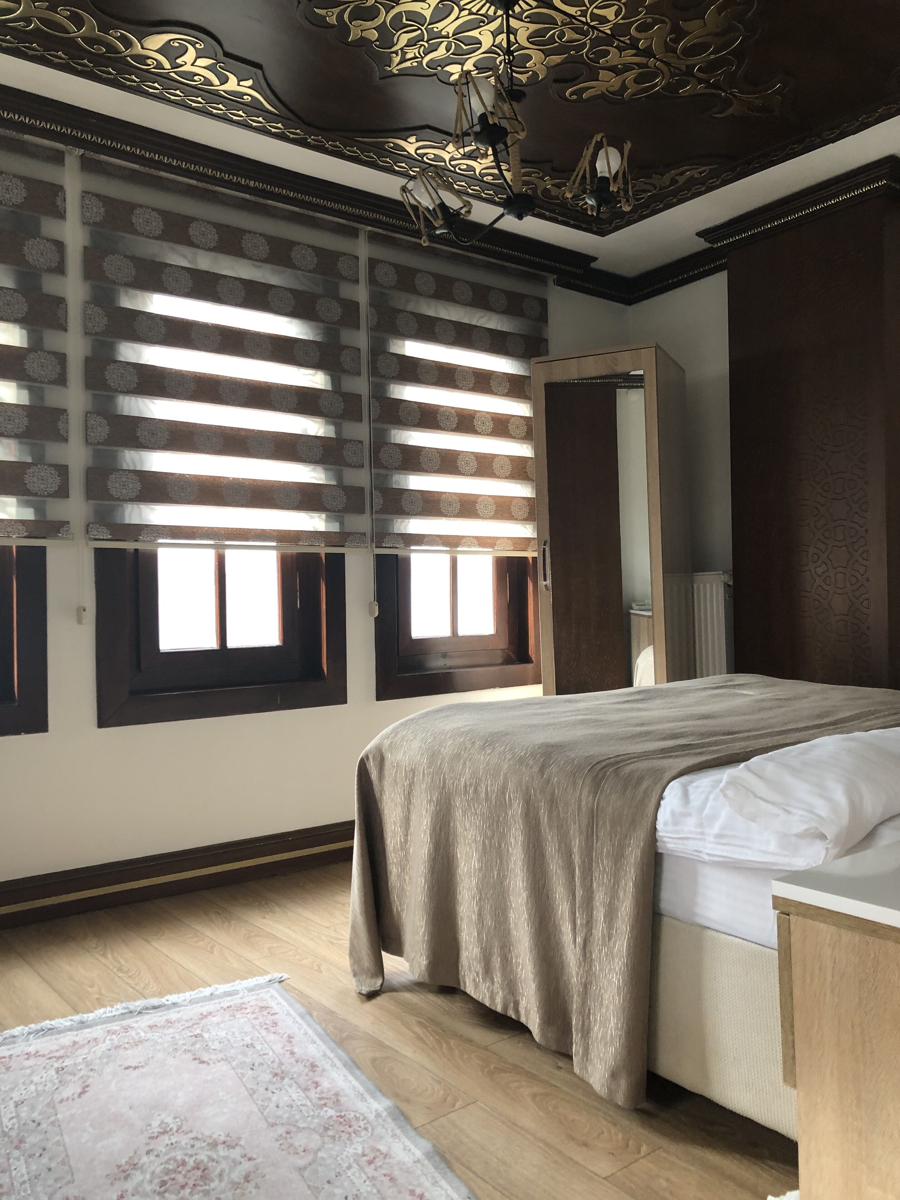 A bedroom with a bed, a wooden floor, a patterned rug, and a decorative ceiling.