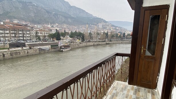 A balcony with a view of a river, a chair, and a table with a metal bowl and spoon.