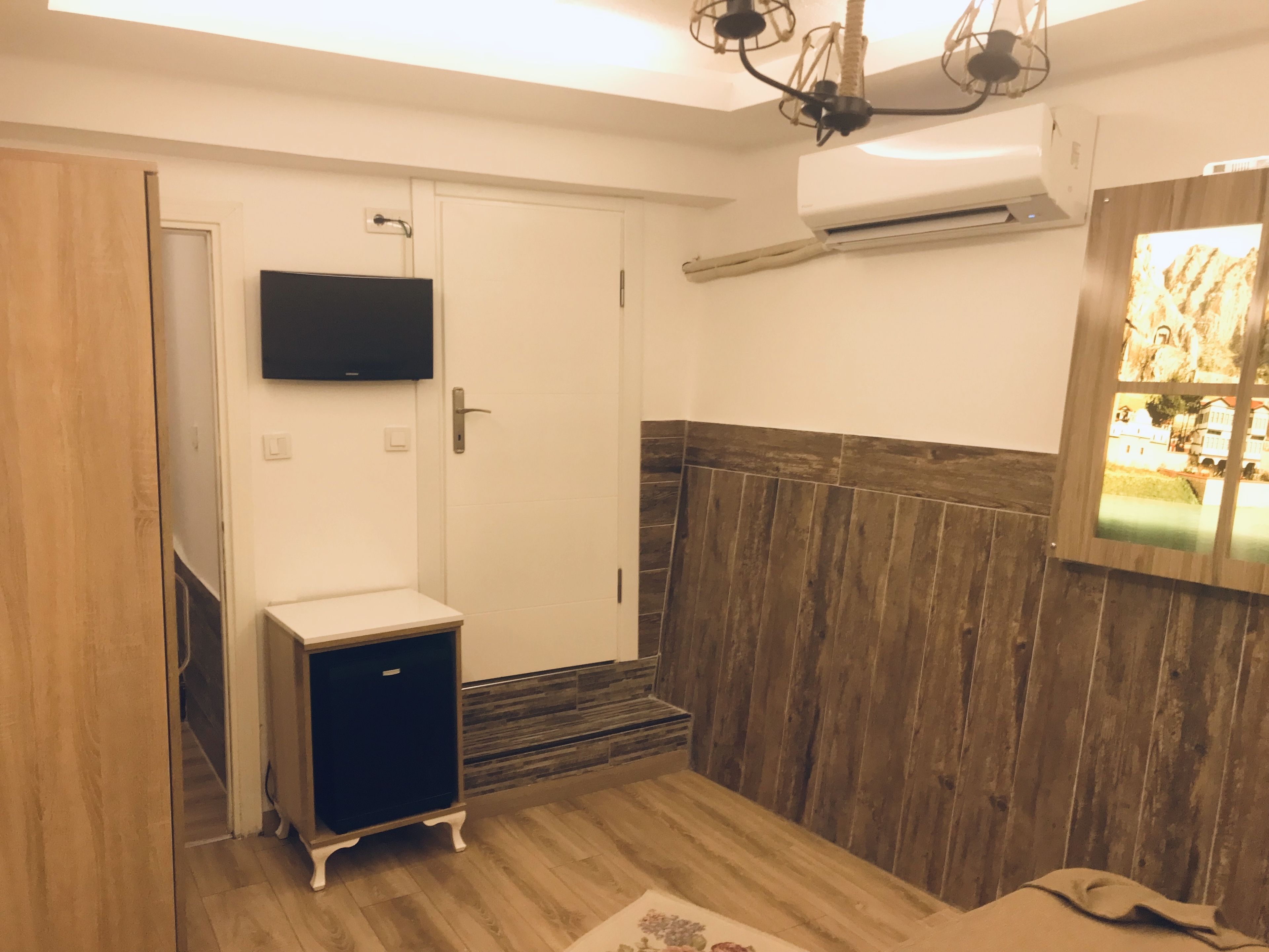 A room with a wooden floor, a small cabinet, a television mounted on the wall, and an air conditioning unit.