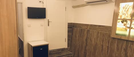 A room with a wooden floor, a small cabinet, a television mounted on the wall, and an air conditioning unit.