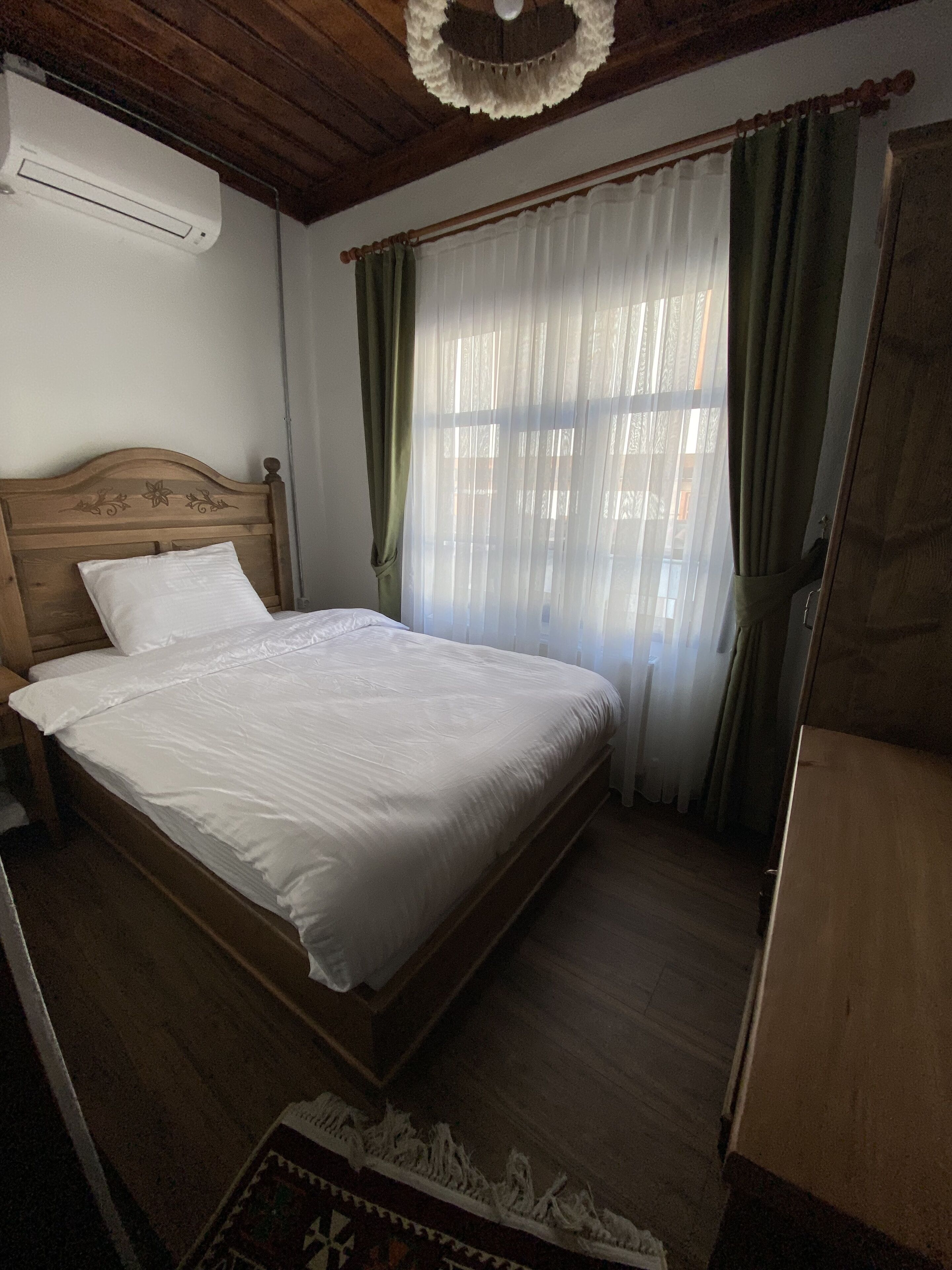 A bedroom with a wooden bed, a nightstand, a dresser, and a window with sheer curtains.
