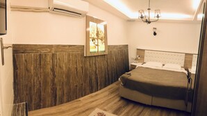 A bedroom with a wooden headboard, a bed with a white headboard, a nightstand, a wall-mounted air conditioner, a chandelier, and a framed picture on the wall.