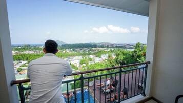 Een man staat op een balkon met uitzicht op een stadsgezicht met gebouwen en groen.