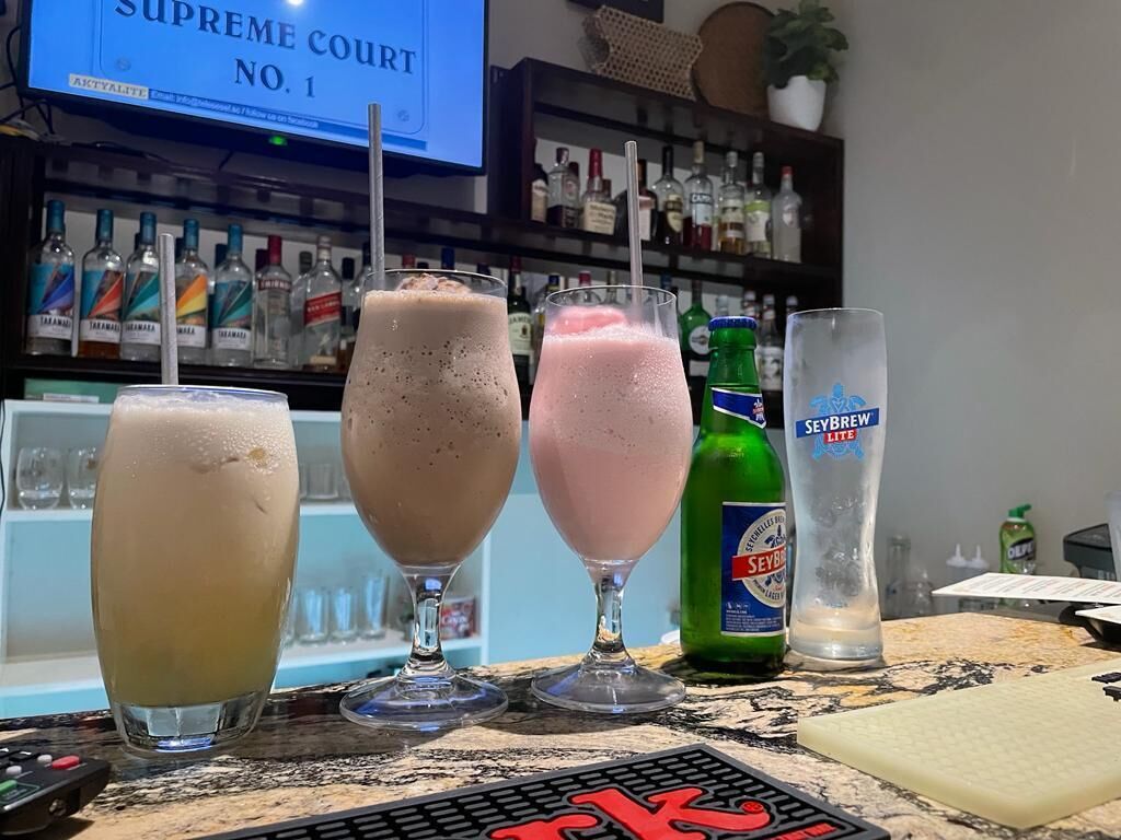 En bar med tre drinks, en flaske Seybrow Lite, og et fjernsyn der viser "SUPREME COURT NO. 1".