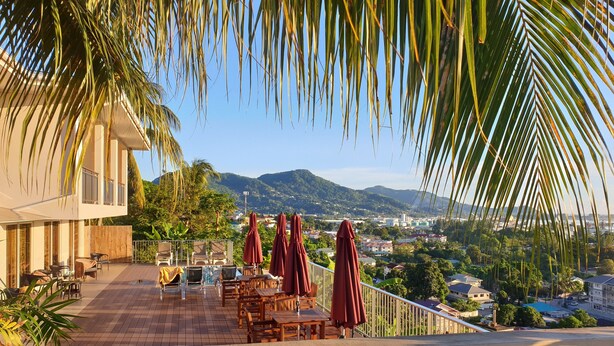 A terrace with outdoor seating and umbrellas, overlooking a scenic landscape with mountains and a town. - The Ridge Residence (Mahé Island)