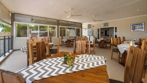A spacious dining area with wooden tables and chairs, large windows, and ceiling fans. - The Ridge Residence (Mahé Island)
