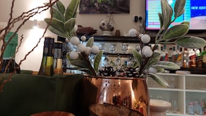 A room with a copper vase containing a plant with white berries, a wooden bowl, and a green cloth. There is a shelf with various items and a television displaying a message. - The Ridge Residence (Mahé Island)