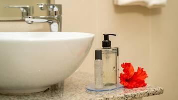 A white sink with a faucet, a small bottle of liquid soap, and a red flower on a granite countertop.