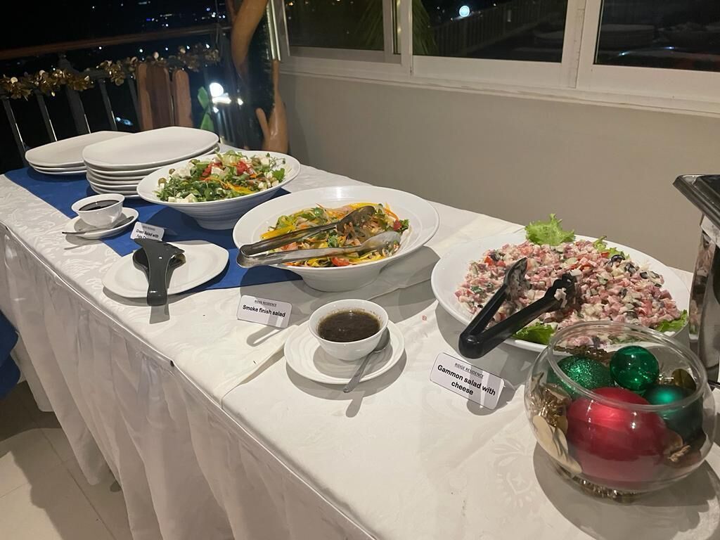 A buffet table with various dishes, including a salad, a pasta dish, and a meat dish, along with condiments and a decorative bowl.