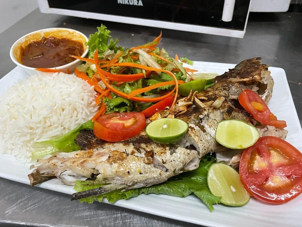 Um prato com peixe grelhado, arroz, salada e fatias de limão.
