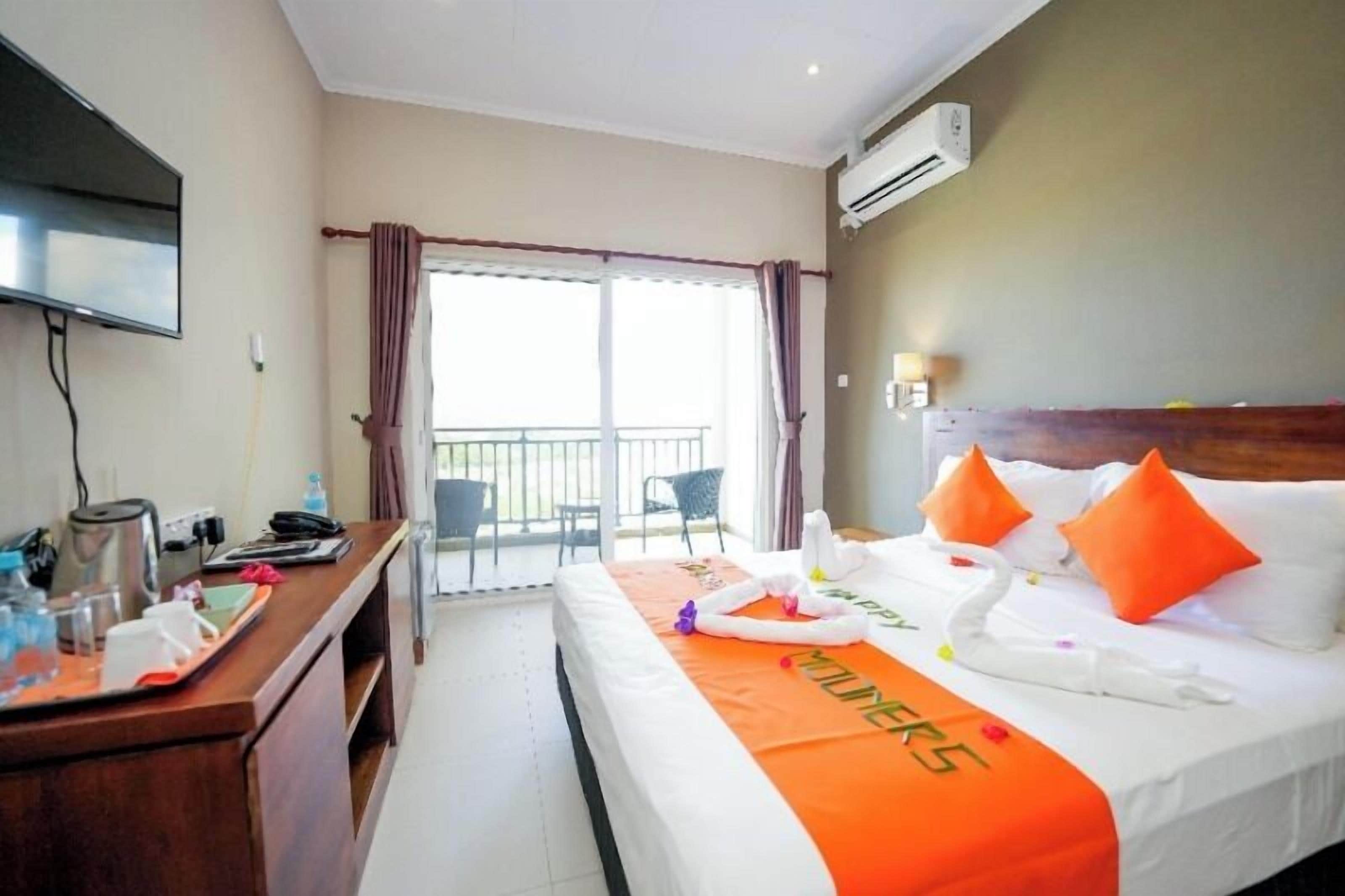 A hotel room with a bed, a desk, a TV, and a balcony.