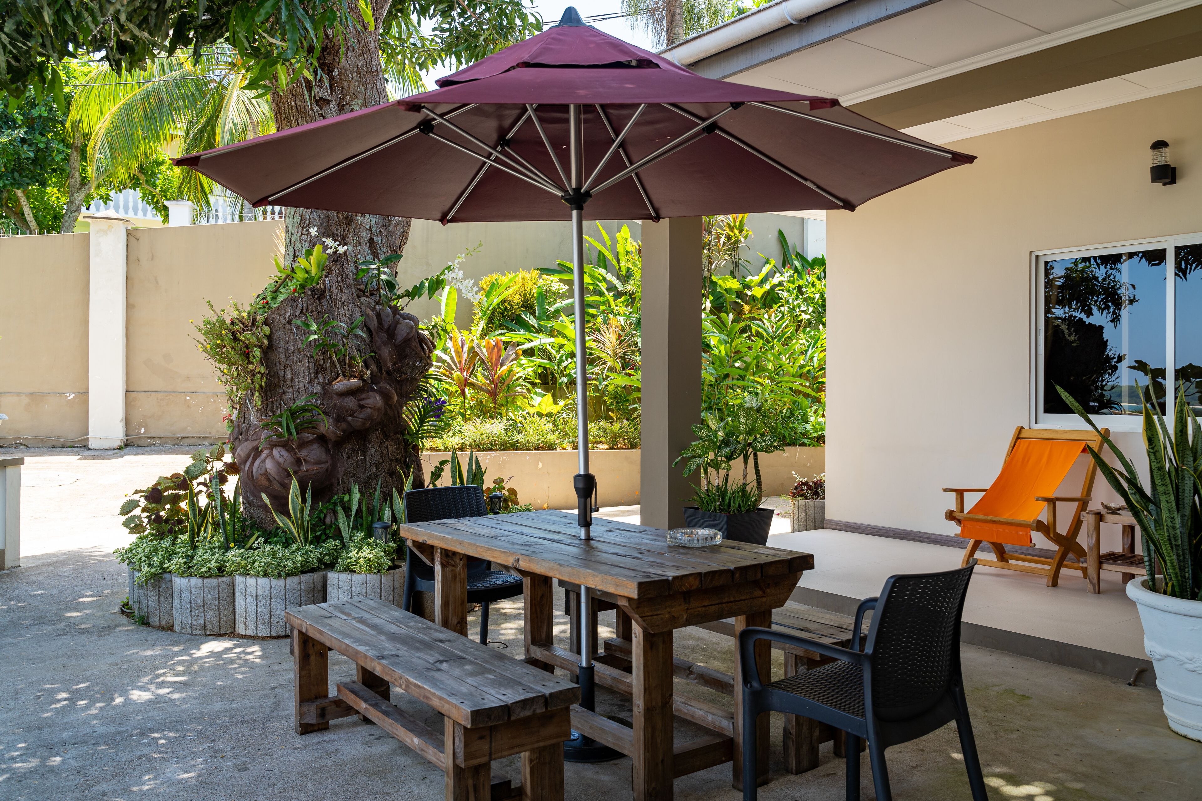 An outdoor patio with a wooden table and benches, an umbrella, and a chair.