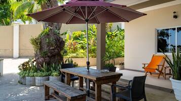 An outdoor patio with a wooden table and benches, an umbrella, and a chair.