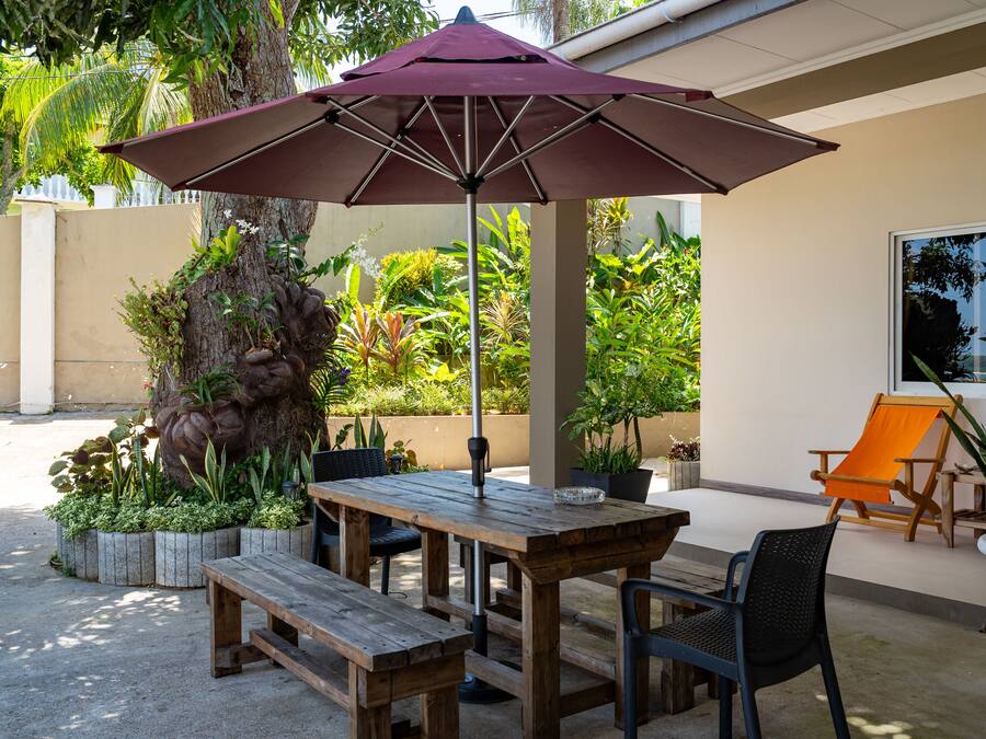 An outdoor patio with a wooden table and benches, an umbrella, and a chair.