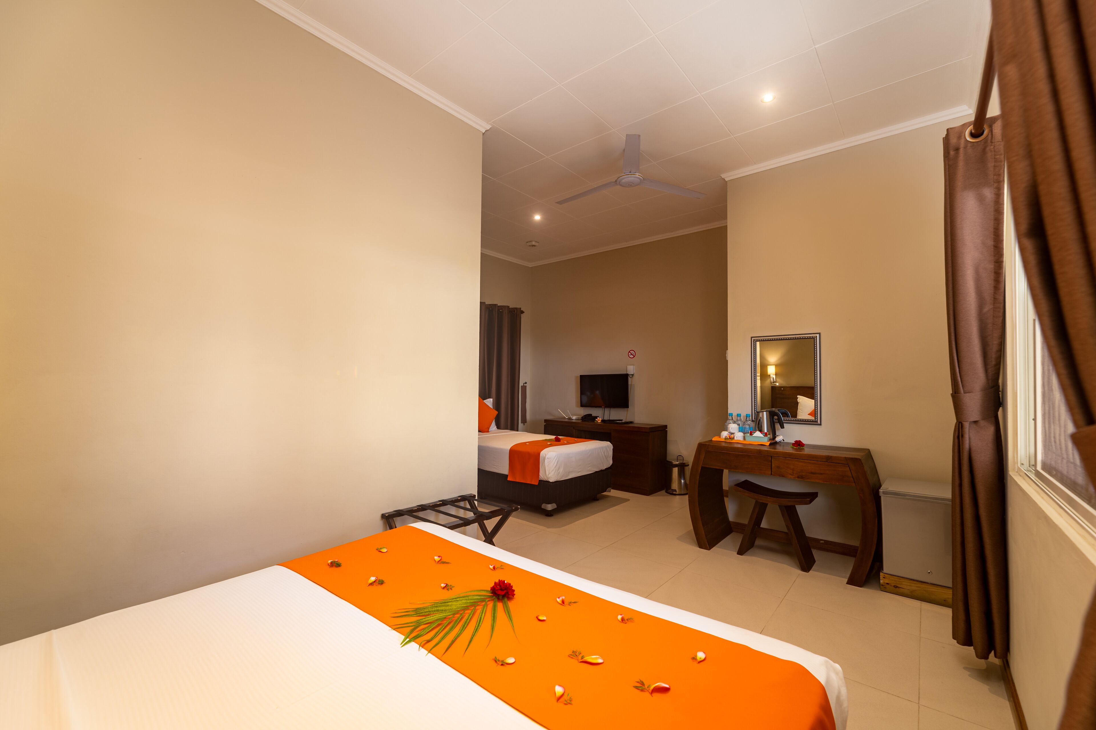 A hotel room with a bed, a desk, a chair, a television, and a ceiling fan.