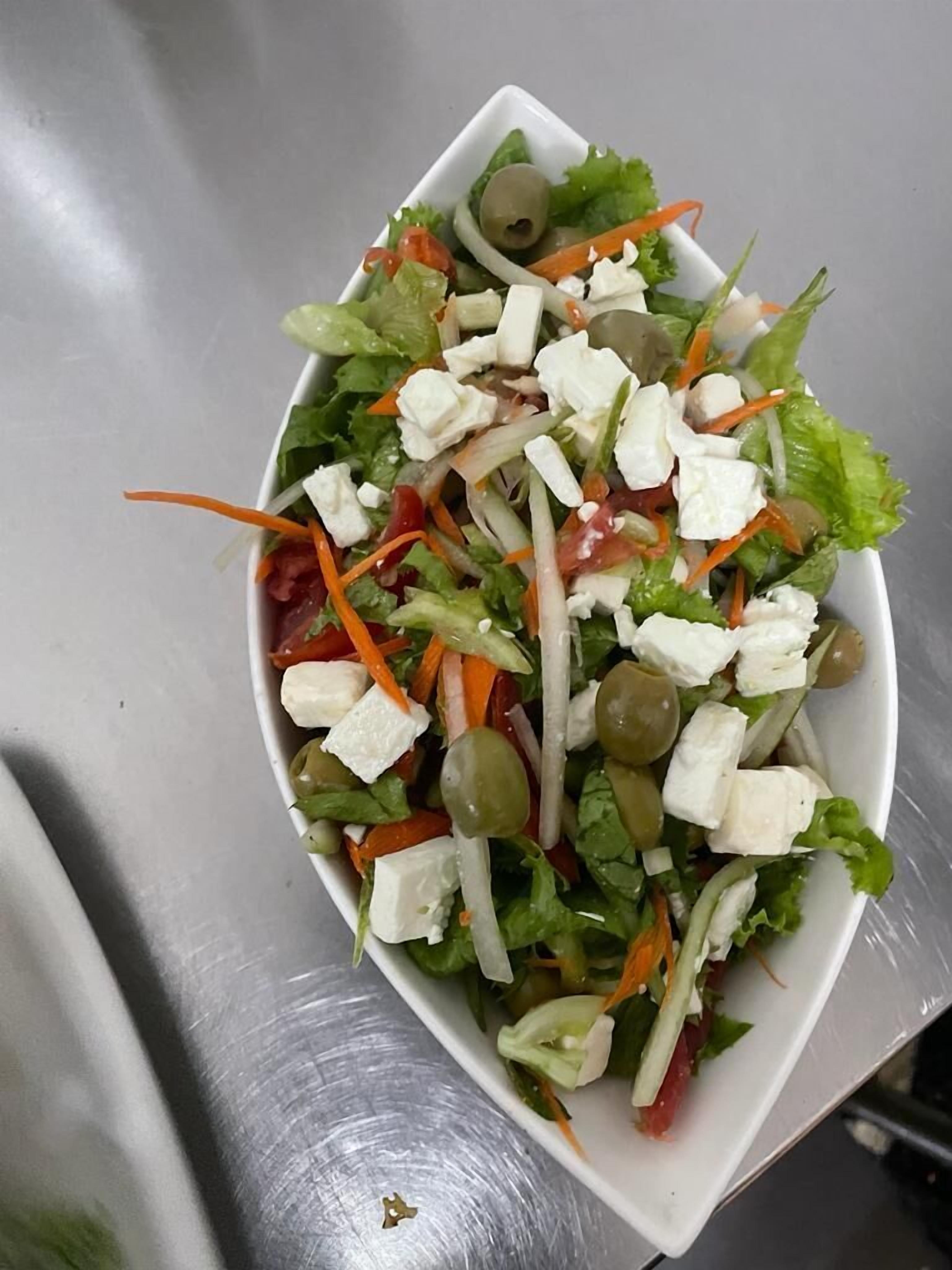 Un plato blanco rectangular con una ensalada de lechuga, zanahorias, aceitunas y queso feta.
