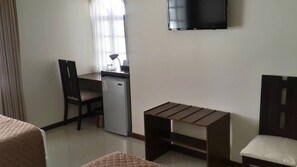 Une petite pièce simple, avec un bureau, une chaise et un téléviseur fixé au mur.