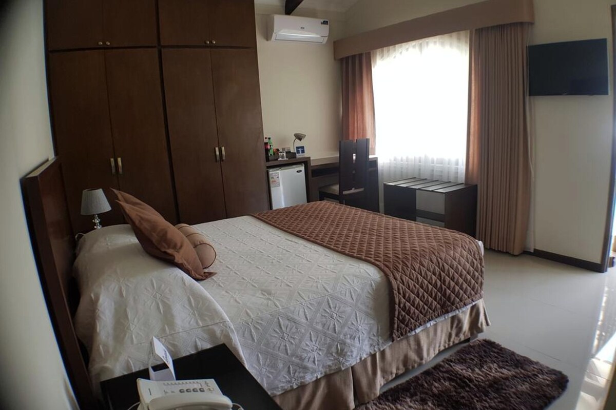 Habitación de hotel con una cama grande, un escritorio, un armario, un televisor y una ventana con cortinas.