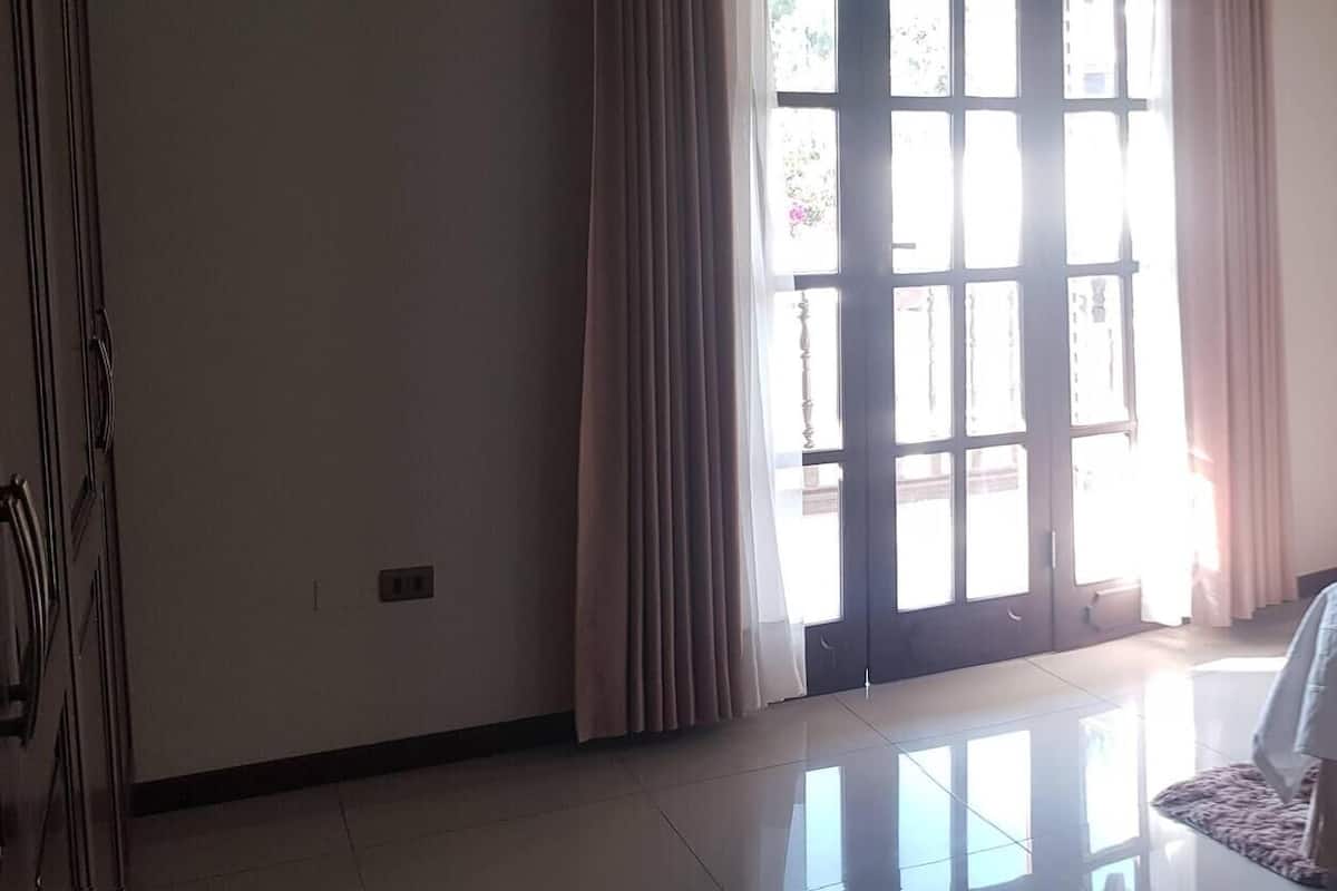 Habitación de hotel con cama, mesita de noche, lámpara, silla y una mesa redonda.