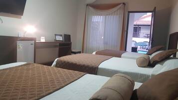 A hotel room with two beds, a desk with a computer, and a window with curtains.