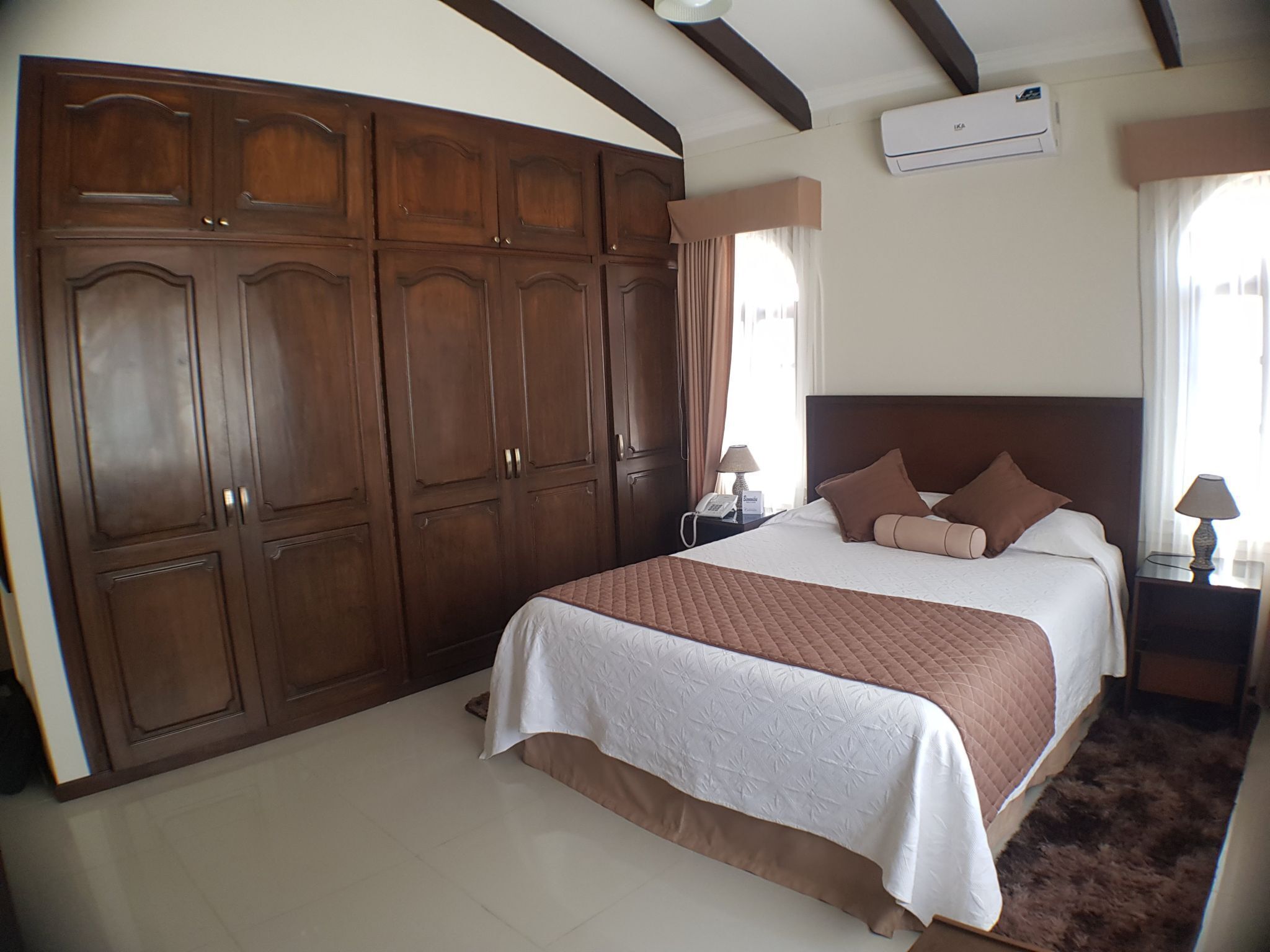 Un dormitorio con un armario de madera grande, una cama con colcha acolchada y una mesita de noche con lámpara.