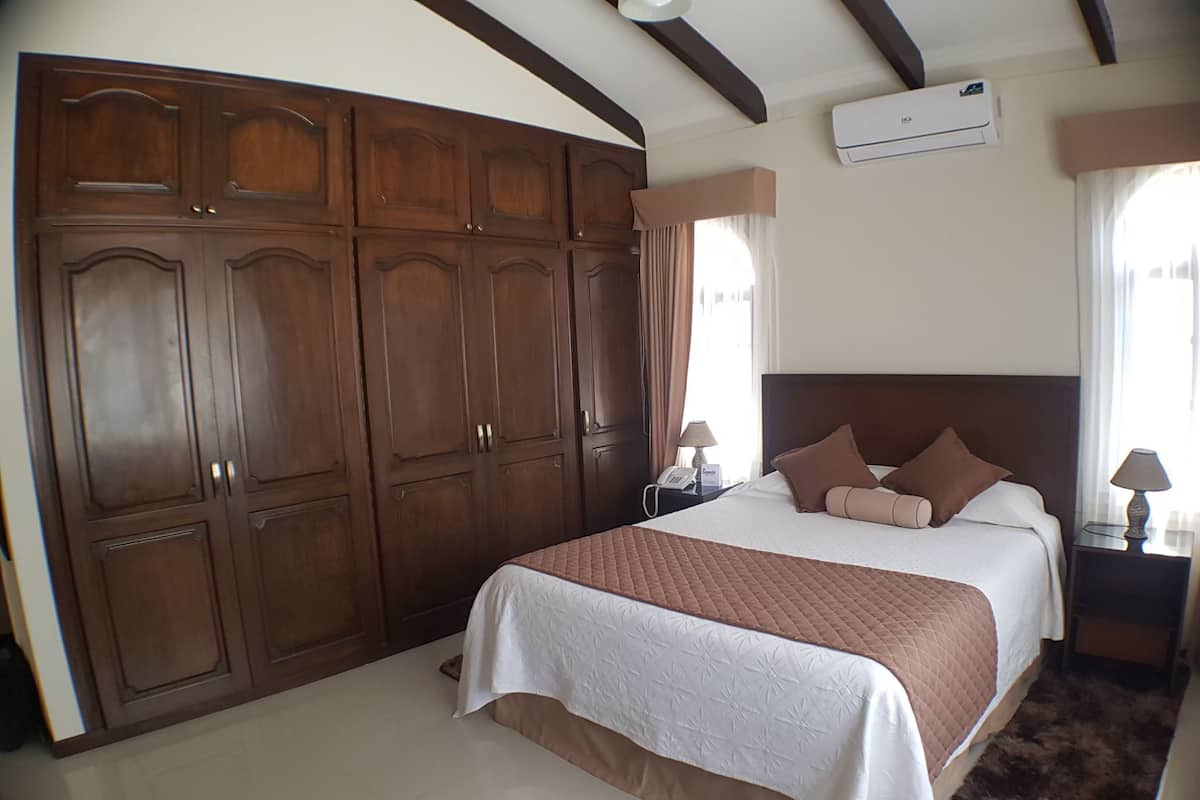 Un dormitorio con un armario de madera grande, una cama con colcha acolchada y una mesita de noche con lámpara.