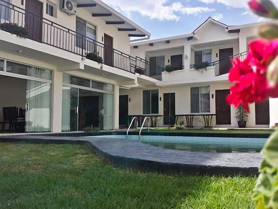 Un hotel moderno de varios pisos con piscina, mobiliario exterior y balcones con plantas.