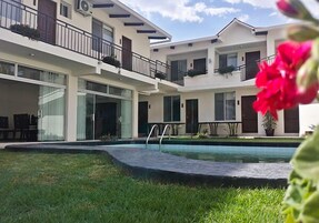 Un hotel moderno de varios pisos con piscina, mobiliario exterior y balcones con plantas.