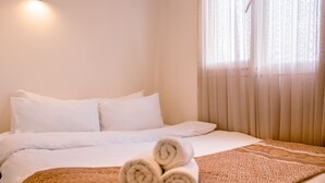A hotel room with a neatly made bed, a rolled towel on the bed, and a window with sheer curtains. - Fi Homes - Adults Only (Izmir)